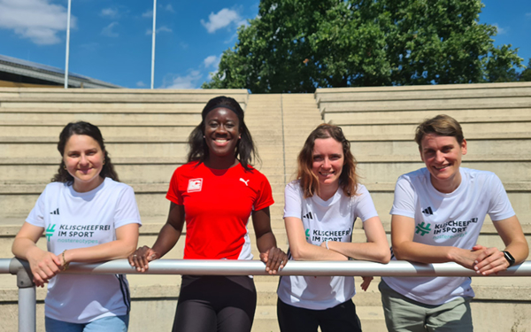 Die Sprinterin Yasmin Kwadwo-Bühner steht mit dem Projektteam von Klischeefrei im Sport vor einer leeren Tribüne.